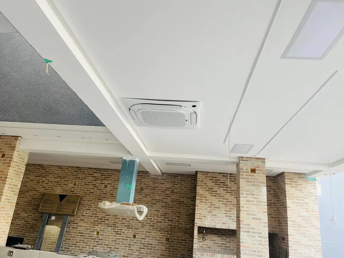 Unidade de ar-condicionado cassete integrada ao forro branco de um ambiente amplo