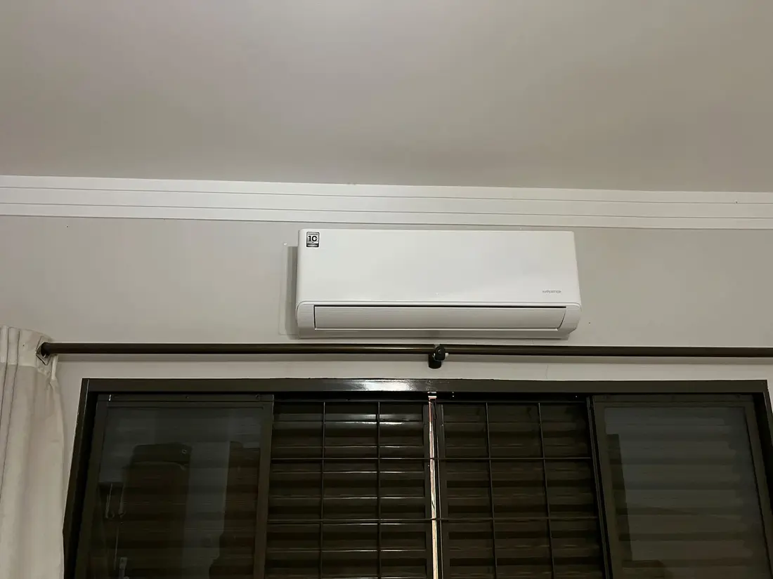 Unidade split branca instalada em uma parede acima de uma janela residencial